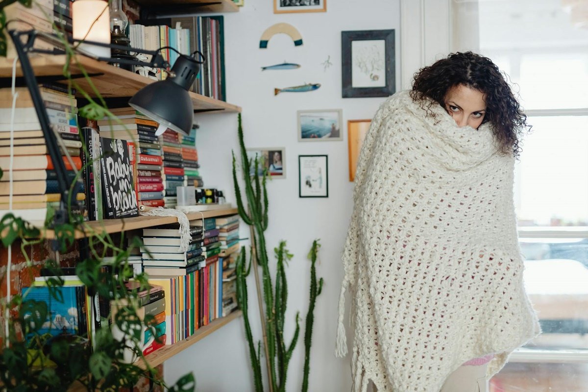 Dark-haired woman wrapped in white shawl beside bookshelves indoors