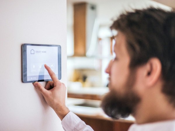 Man adjusting indoor temperature on wall-mounted thermostat