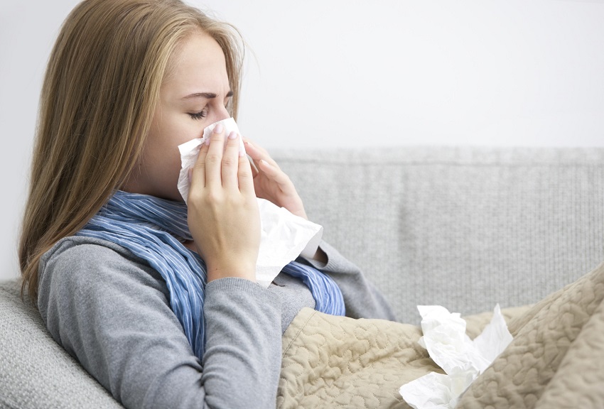 Blond woman blowing nose on couch of home