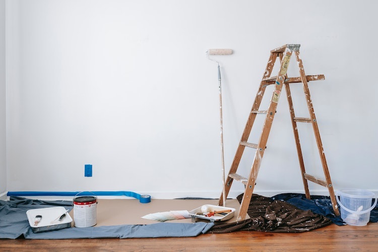 Newly painted white room with paint roller, paint tray, wooden ladder and masking tape partially peeled from wall