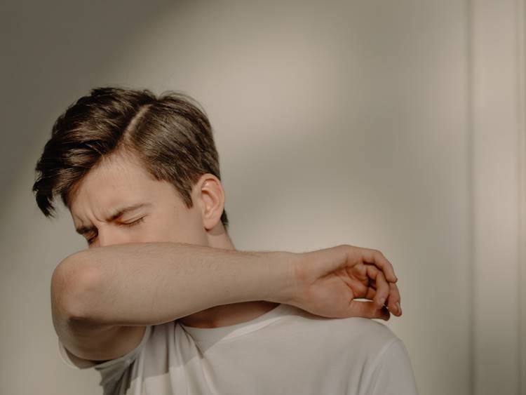 Short-haired man sneezing into elbow in white sunlit room