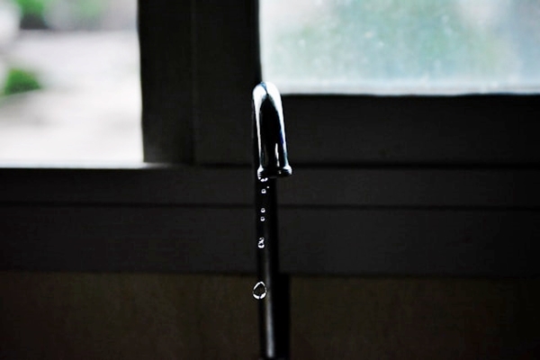 Dripping stainless steel faucet beside kitchen window