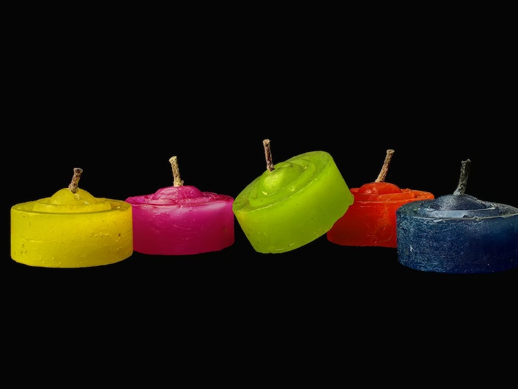 Five paraffin votive candles in assorted colors photographed against black background