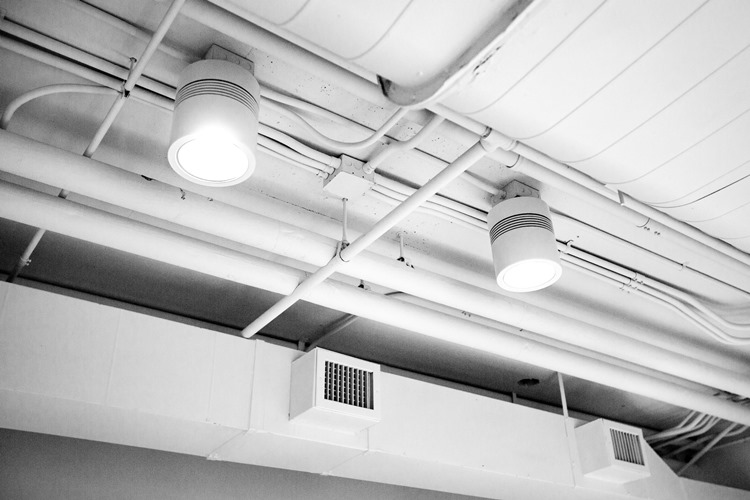 Exposed white ducts on ceiling with two large overhead lights