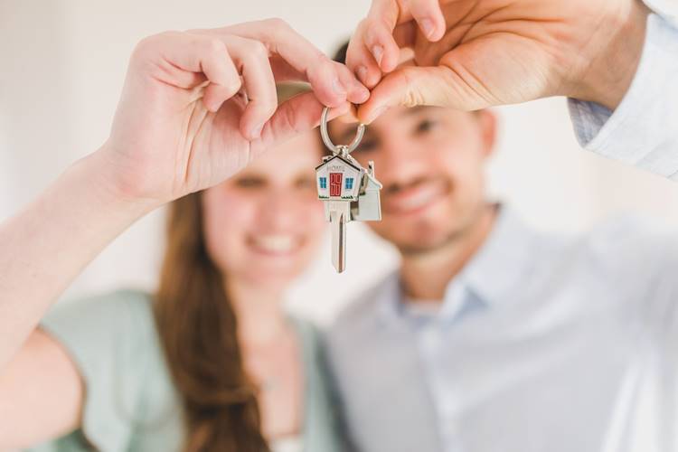Smiling couple holding keychain with single key and house-shaped charm