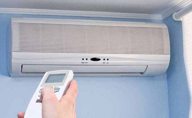 Homeowner pointing remote control at white wall-mounted air conditioner unit