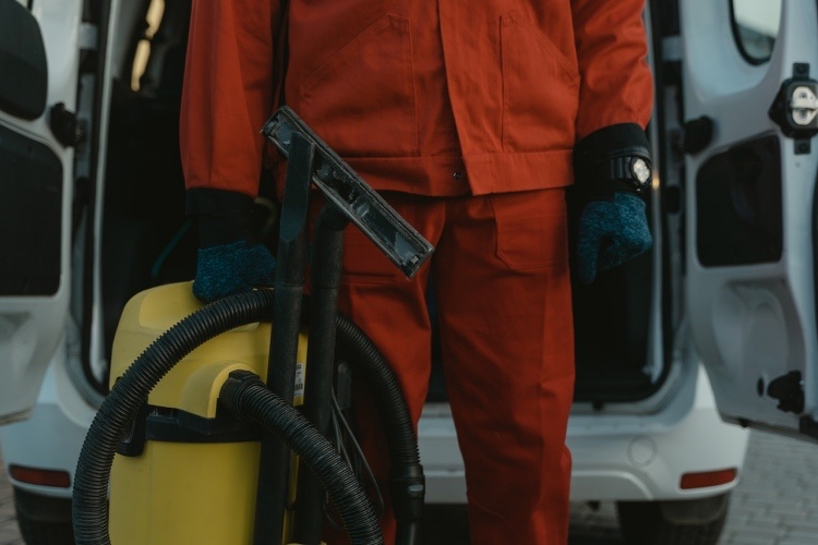 Professional cleaning technician in orange bodysuit holding vacuum cleaner behind service van