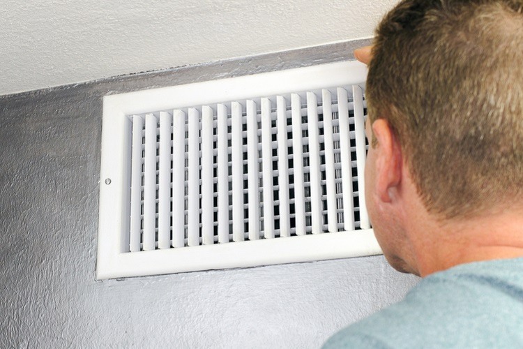 Homeowner adjusting air vent on upper wall of home