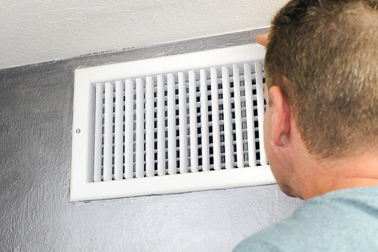 Homeowner adjusting air vent on the upper wall of home